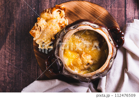 Close up of french onion soup with melted cheese and croutons in a pot on the table top view Close up of french onion soup with melted cheese and croutons in a pot on the table top view 112476509