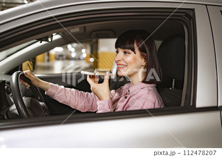 Female records audio messages using phone inside vehicle on underground parking. Female records audio messages using phone inside vehicle on underground parking. 112478207