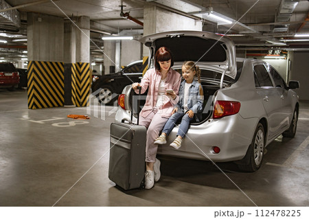 Mother and daughter sitting in trunk of modern car in underground parking lot. 112478225