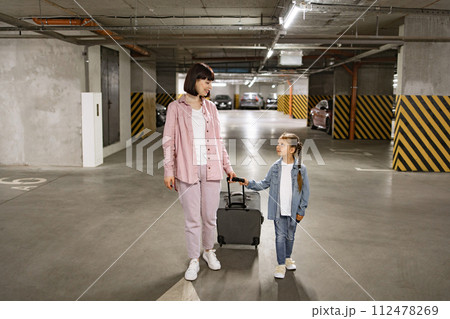 Caucasian mother and little daughter walking through underground parking lot. 112478269
