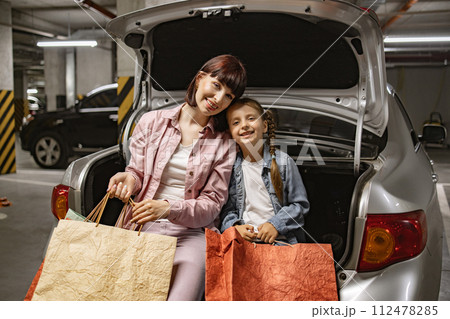 Caucasian mother and small daughter sitting on open trunk of modern car. Caucasian mother and small daughter sitting on open trunk of modern car. 112478285