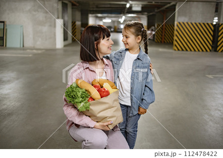 Mother and daughter in casual clothes holding paper bag with vegetables. Mother and daughter in casual clothes holding paper bag with vegetables. 112478422