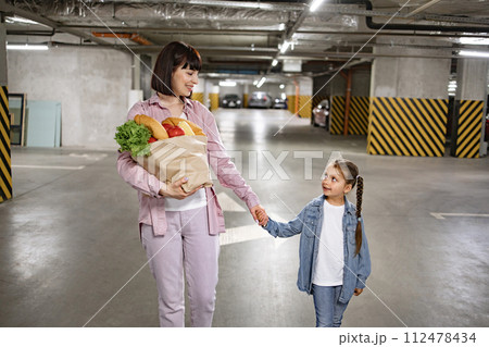 Mother and daughter walking and holding paper bag with vegetables. Mother and daughter walking and holding paper bag with vegetables. 112478434