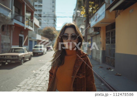 A woman in a brown jacket and sunglasses stands on a city street 112478586