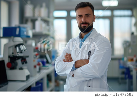 A man in a white lab coat stands in front of a lab bench with a serious expressi 112478593