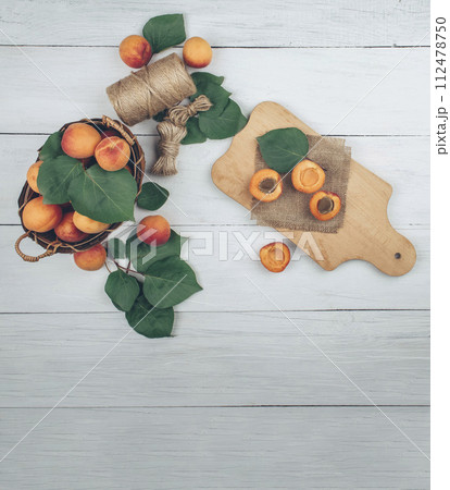 Ripe apricots and apricot leaves in a bowl on a wooden table. Fresh fruit. Healthy food. Flat lay 112478750