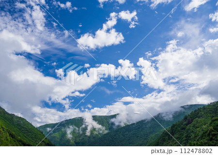 夏空に沸き立つ白い雲と山並み 112478802