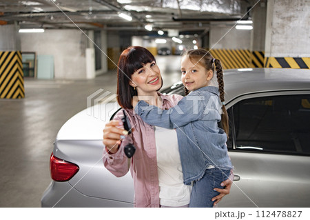 Happy Caucasian woman holding female kid and car keys in underground parking lot Happy Caucasian woman holding female kid and car keys in underground parking lot 112478827