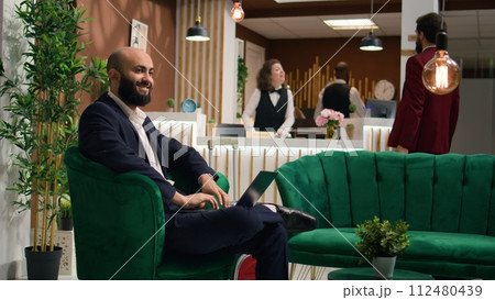 Middle eastern worker on business trip writing presentation notes in lounge area, meeting with investors abroad. Executive manager working on laptop reviewing notes, travelling for work. 112480439