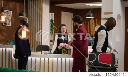 Hotel staff offering luxury services to businessmen guests at resort, travelling on business trip and attending international conference. Managers team doing check in at front desk reception. Hotel staff offering luxury services to businessmen guests at resort, travelling on business trip and attending international conference. Managers team doing check in at front desk reception. 112480441