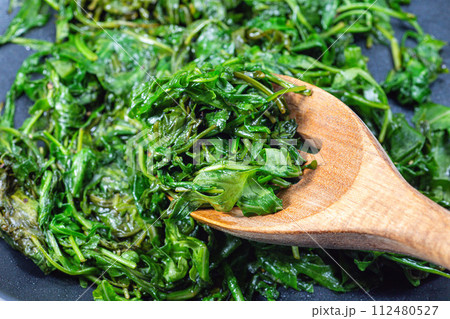 Wilted arugula or rocket salad, preparing a side dish in frying pan, horizontal closeup 112480527