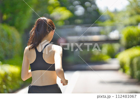 緑の中をランニングするスポーツウエアの若い女性の後ろ姿 112481067