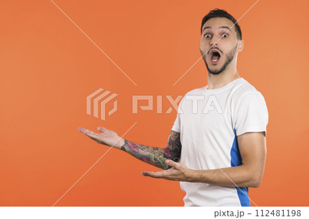 Young male soccer player or fan presenting a product on the side with stretched arms. Copy space 112481198