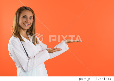 Beautiful female doctor or nurse in white coat presenting a product with copyspace Beautiful female doctor or nurse in white coat presenting a product with copyspace 112481233