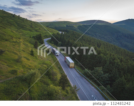 Truck of delivery company with cargo is driving on forest road in the mountains at sunset 112481242