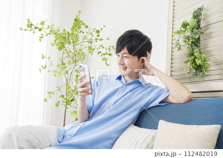 リビングルームでスマホを使う若い男性 リビングルームでスマホを使う若い男性 112482019