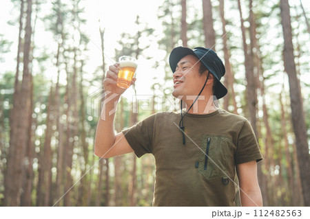 キャンプ場でビールを飲む男性キャンパー（お酒・アルコール・クラフトビール・発泡酒） 112482563