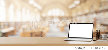 A laptop computer mockup on a wooden desk with a blurred background of a beautiful spacious library. 112483147