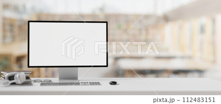 A white-screen computer mockup on a table with a blurred background of a contemporary library. 112483151