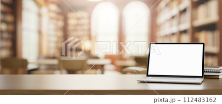 A white-screen laptop computer mockup and books on a wooden table in a beautiful vintage library. A white-screen laptop computer mockup and books on a wooden table in a beautiful vintage library. 112483162