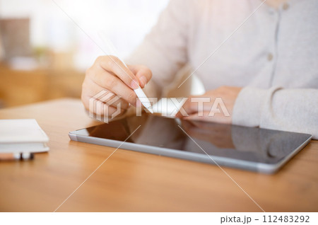 A cropped shot of a woman working on her digital tablet at a table indoors or in a minimalist cafe. A cropped shot of a woman working on her digital tablet at a table indoors or in a minimalist cafe. 112483292