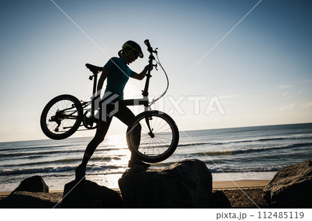 Woman taking a folding bike on sunrise seaside 112485119