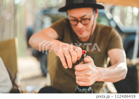 キャンプ場でワインのコルクを開ける男性キャンパー（栓抜き・ワインオープナー） 112486439