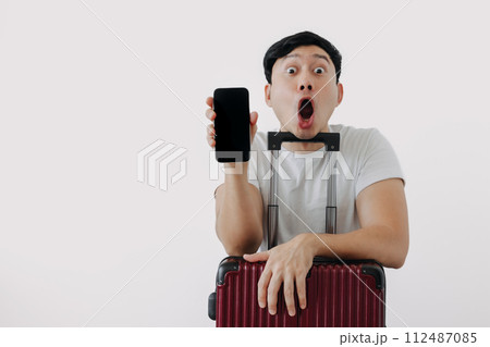 Shock and surprise face of man using mobile phone application for travel, sitting with his baggage or luggage. 112487085