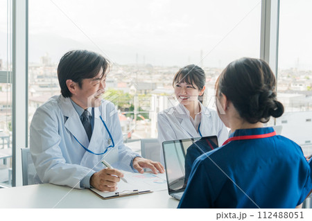 医局でカンファレンス・打ち合わせ・ミーティングする男女の医師・医者・看護師・医療従事者・技師 112488051