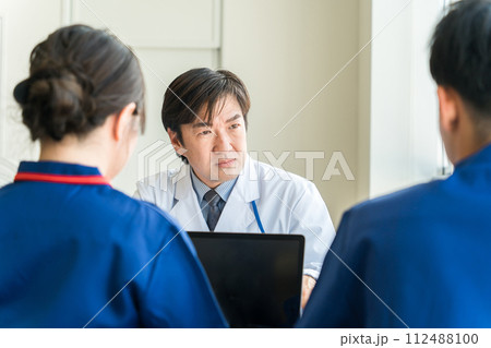医療スタッフ・医療従事者の相談を真剣な表情で聞く男性医師・教授 112488100