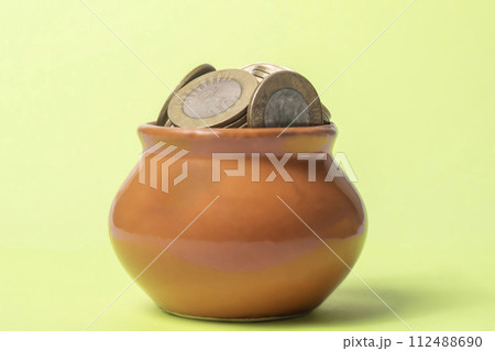 Coins in a clay pot on a green background. Money saving concept. 112488690