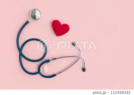 World Heart Day. Heart as a symbol of health, treatment, cardiology on a pink background with a medical statoscope. View from above. Global health concept. Listen to your heart 112489382