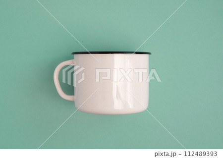 White blank vintage enamel mug isolated on green color studio background. Retro style steel cup, empty mock-up. Banner. Copy space. Place for logo, text, advertising. Tourism, hiking, journey White blank vintage enamel mug isolated on green color studio background. Retro style steel cup, empty mock-up. Banner. Copy space. Place for logo, text, advertising. Tourism, hiking, journey 112489393