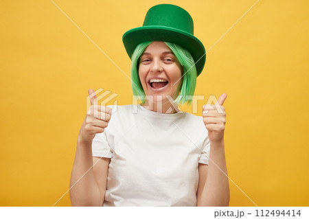 Enjoying for St. Patrick's Day celebrations. Delighted Caucasian woman wearing green leprechaun hat standing isolated over yellow background showing thumb up like gesture Enjoying for St. Patrick's Day celebrations. Delighted Caucasian woman wearing green leprechaun hat standing isolated over yellow background showing thumb up like gesture 112494414