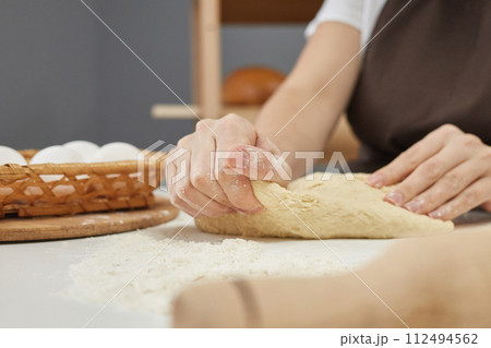 Unknown baker hands kneading dough for making homemade pastry or baking bread while sitting at workplace in bakehouse Unknown baker hands kneading dough for making homemade pastry or baking bread while sitting at workplace in bakehouse 112494562