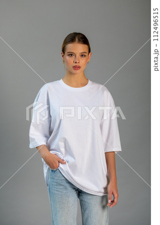 Beautiful blonde girl in a white oversized T-shirt and blue jeans posing on a gray background 112496515