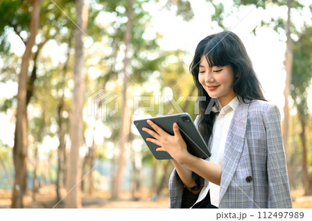 Young businesswoman using digital tablet while sitting on bench in the autumn park 112497989