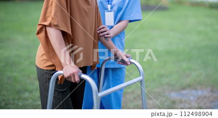 Nurse or caregiver hand on walking frame for support, help or trust moving leg in rehabilitation. Physiotherapy healthcare, Medical caregiver consulting disabled elderly patient at home Nurse or caregiver hand on walking frame for support, help or trust moving leg in rehabilitation. Physiotherapy healthcare, Medical caregiver consulting disabled elderly patient at home 112498904