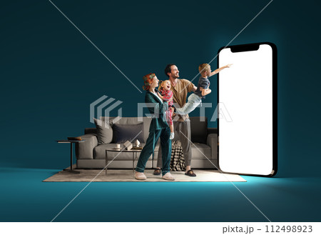Family interacting with huge 3D model of smartphone in living room against blue background. Online shopping, delivery services, sales 112498923