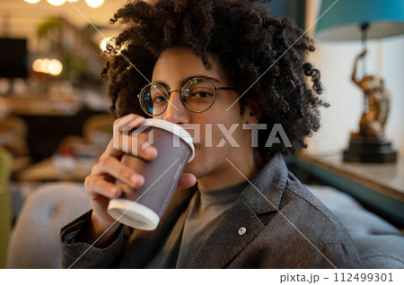 Young curly-haired man sitting in a hotel hall and drinking coffee 112499301