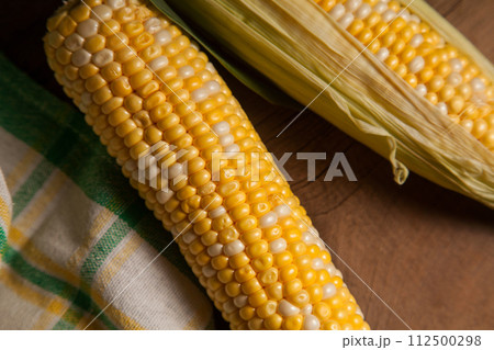 Close up view of three cobs sweet corn with green leaves on wooden background.. 112500298