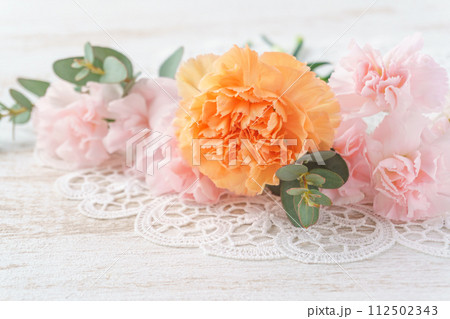 白い木目背景にピンクとオレンジのカーネーションとユーカリのアレンジメント 112502343