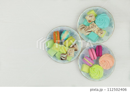 Various desserts. Sweet desserts in plates for holiday. Macaroons, marshmallows and zephyrs on a white background. Top view. Various desserts. Sweet desserts in plates for holiday. Macaroons, marshmallows and zephyrs on a white background. Top view. 112502406