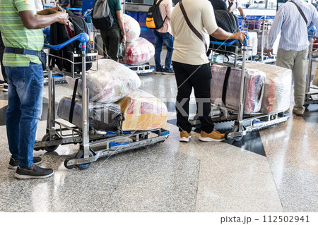 Passenger travelers at airport with luggages on trolley wrapped with protective film 112502941