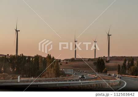 Sky high wind turbines line the highway, blending nature with infrastructure Sky high wind turbines line the highway, blending nature with infrastructure 112503642