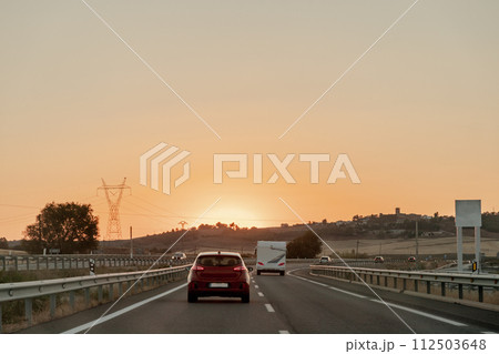 Vehicle on asphalt road, under sunset sky, driving on thoroughfare 112503648