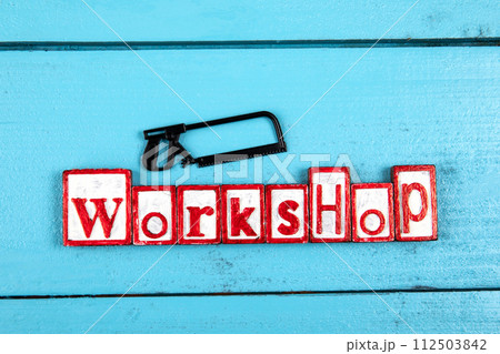 WORKSHOP. Miniature saw on a blue wooden background. Construction and carpentry concept WORKSHOP. Miniature saw on a blue wooden background. Construction and carpentry concept 112503842