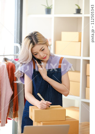 Online shopping concept, Female entrepreneur talks on smartphone and writes address on parcel boxes. Online shopping concept, Female entrepreneur talks on smartphone and writes address on parcel boxes. 112505343