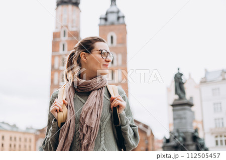 Tourist happy woman in glasses on Market Square in Krakow, Traveling Europe in autumn. St. Marys Basilica, cloudy day 112505457