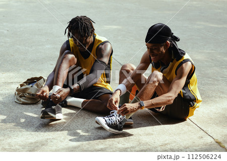 Cheerful Black men tying shoe laces before game of streetball Cheerful Black men tying shoe laces before game of streetball 112506224
